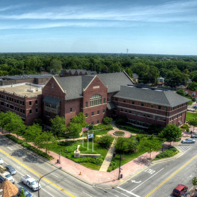 Aerial drone shot of Village Hall building and sign shown from corner of Main Street and Busse Avenue on a sunny day.