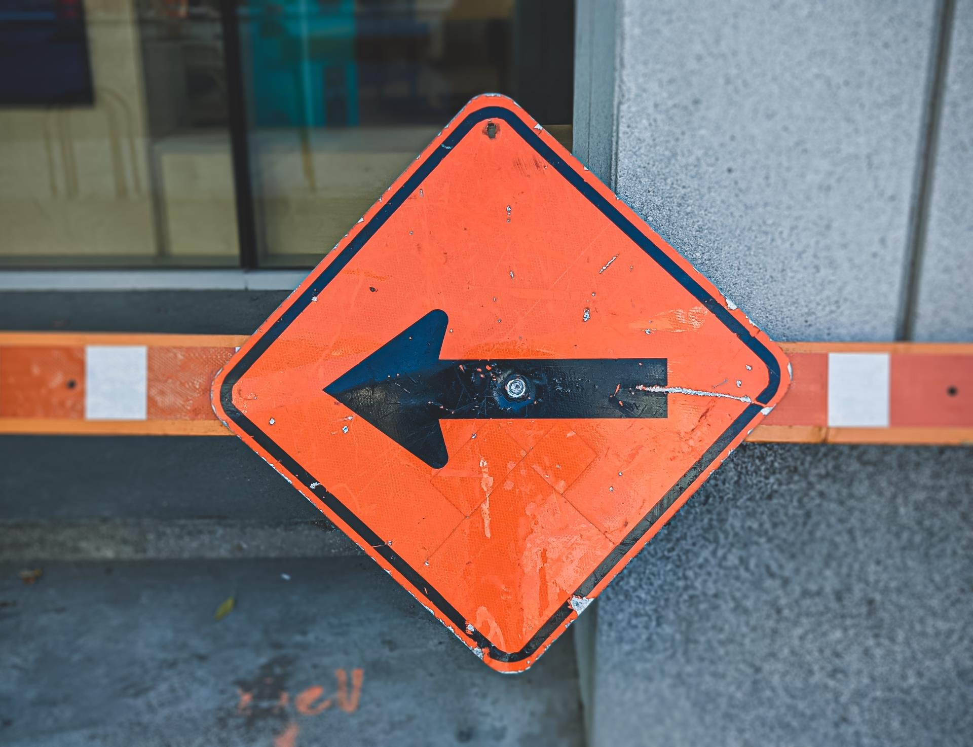 Close up of an orange construction sign with an arrow pointing left.