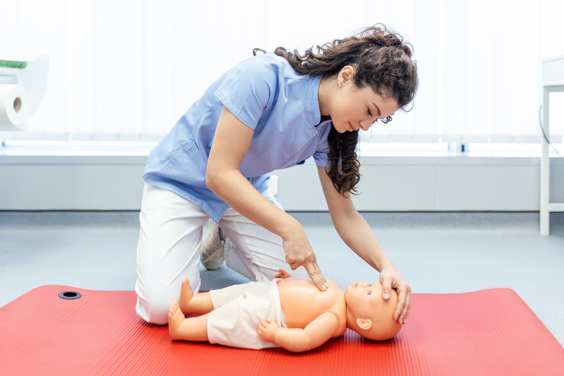 woman applying chest compressions to a CPR baby mannequin 